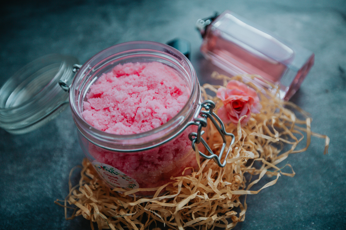 Pink body scrub in glass bottle placed on table with perfume bottle
